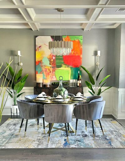 A modern dining room with a round table, velvet chairs, abstract artwork, and decorative lighting.