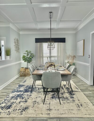 A modern dining room featuring a rectangular table set for six, with upholstered chairs, a two-tone area rug, and a stylish pendant light.