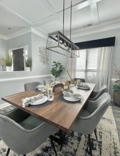A modern dining room with a wooden table set for a meal, upholstered chairs, and stylish pendant lighting.