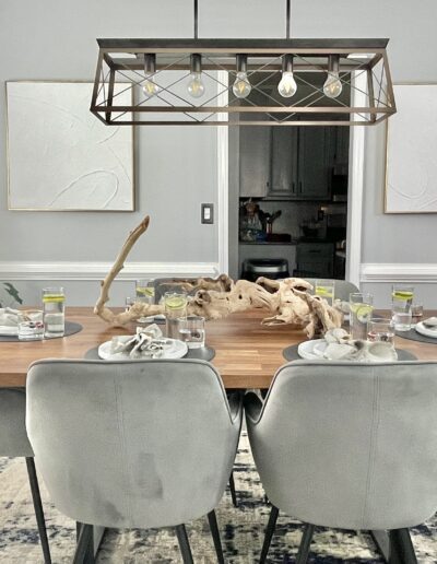 A modern dining room setup with a wooden table, six grey chairs, and an elegant chandelier.