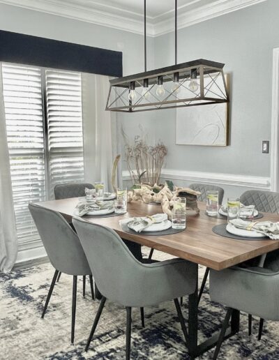 A neatly set dining table in a modern room with gray walls, white curtains, and decorative elements.