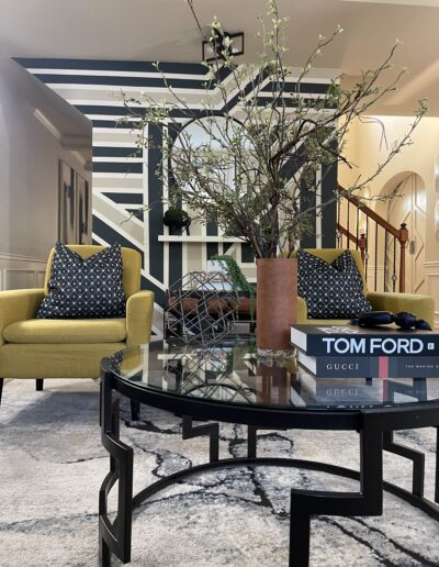 A stylish interior with chartreuse armchairs, patterned pillows, and a modern coffee table featuring books and a vase with branches.