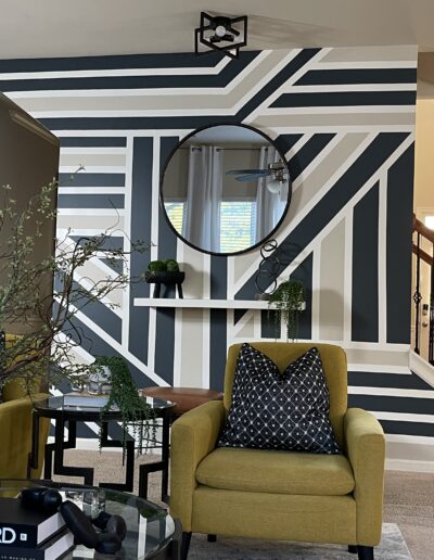 A stylish living room with a bold black and white striped accent wall, featuring modern furniture and decorative items.