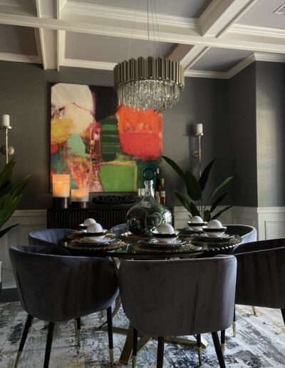 Modern dining room with an abstract painting, crystal chandelier, and a round table set for dinner.