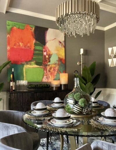 Elegant dining room with a modern art painting, crystal chandelier, and a decorated table.
