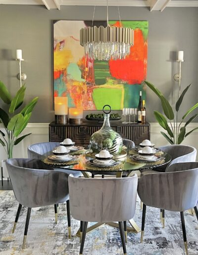 A modern dining room featuring a glass table with plush chairs, vibrant abstract art, and decorative plants.