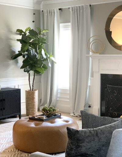 A cozy living room with neutral tones, featuring a fireplace, a mounted tv, and comfortable seating arranged around a leather ottoman.