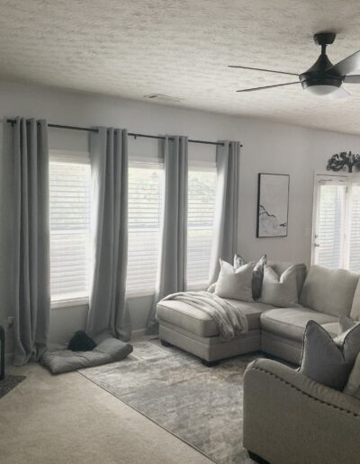 A well-lit, cozy living room with a sectional sofa, fireplace, and ceiling fan.
